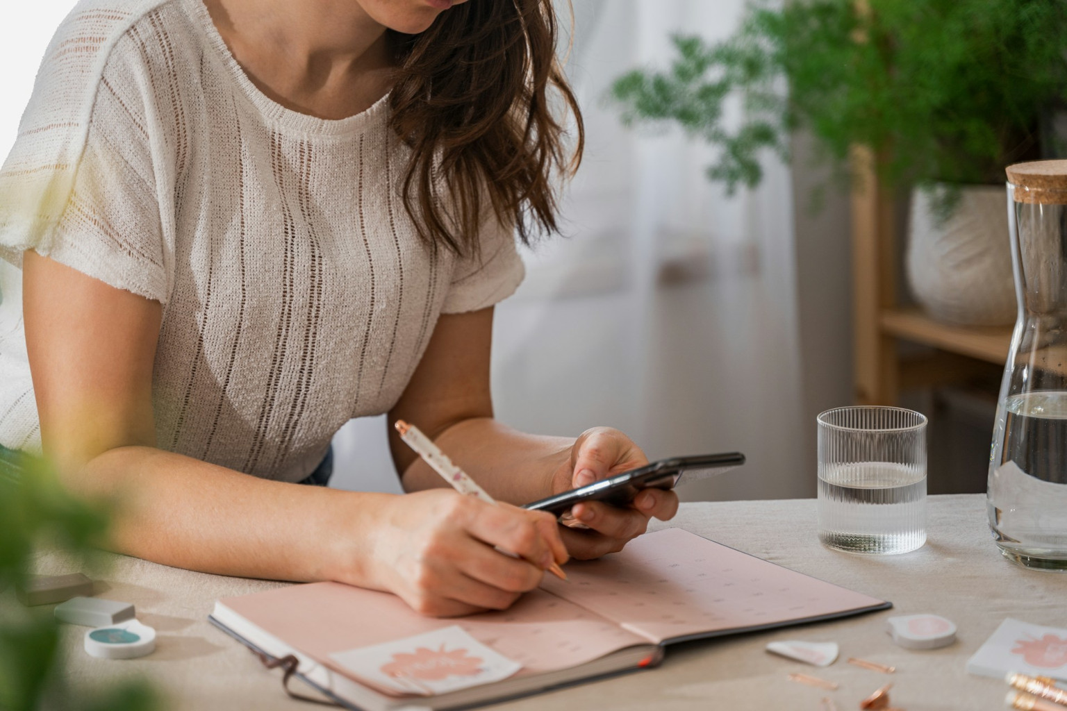 A woman looking at her phone while writing in a notebook, trying to coordinate plans